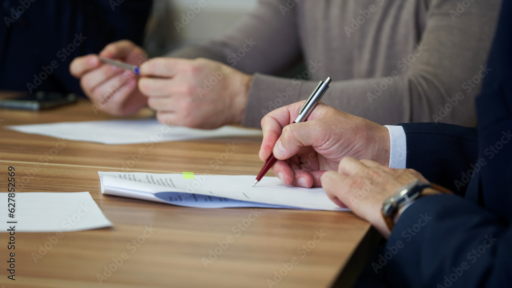 A man signs a document during a business meeting or negotiations. Signing an order, deal, memorandum, agreement or contract. No face. Selective focus
