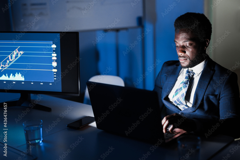 African man trader working at night time inside hedge fund bank office - Trading, investment and business concept - Focus on face