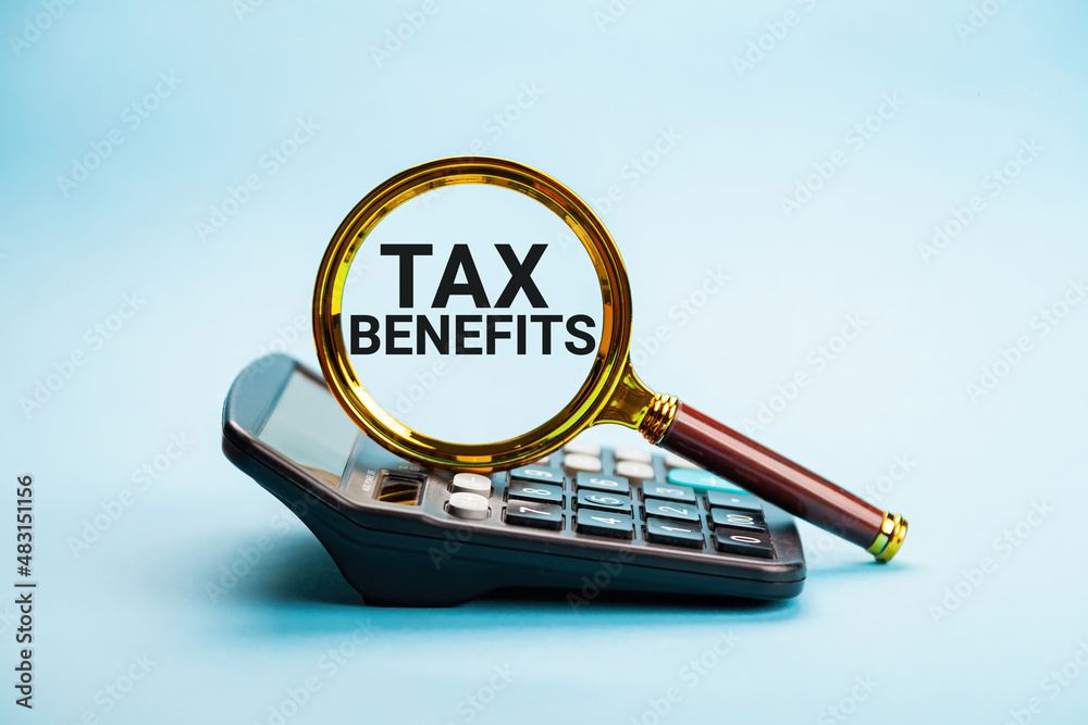 TAX BENEFITS. The concept of finance and business. On the blue background lies a calculator and a magnifying glass with the inscription - TAX BENEFITS. Planning budget, using calculator checking