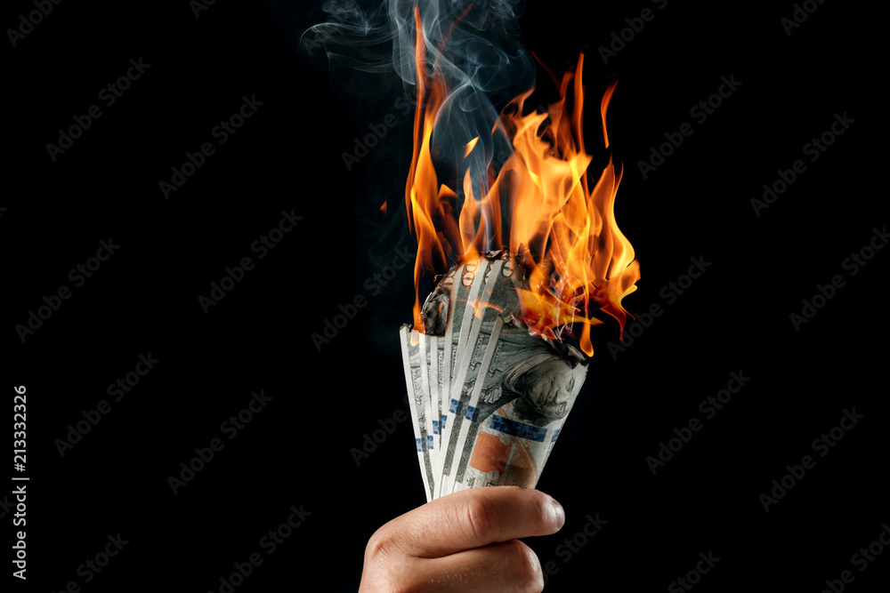 Male hand close-up, holds burning money in hands, burning US dollars. Black background, isolate. The concept of inflation, a decrease in the purchase of foreign currency, and devolution.